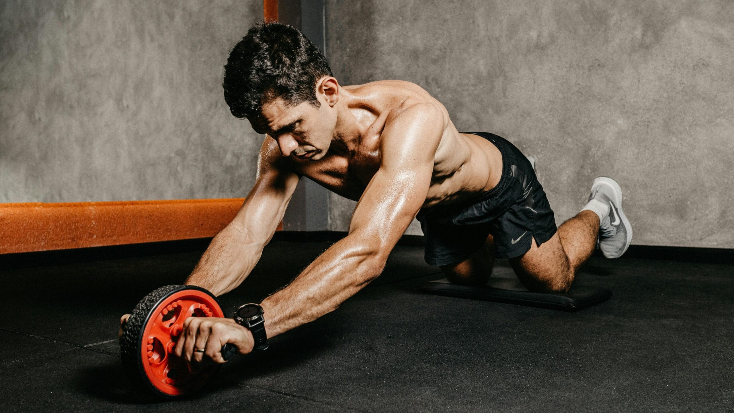 Muscular man exercising with an ab roller for core strength in an indoor gym setting, showcasing athletic fitness.